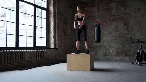 mujer atlética en forma hace saltos de caja en el gimnasio de la fábrica desierta