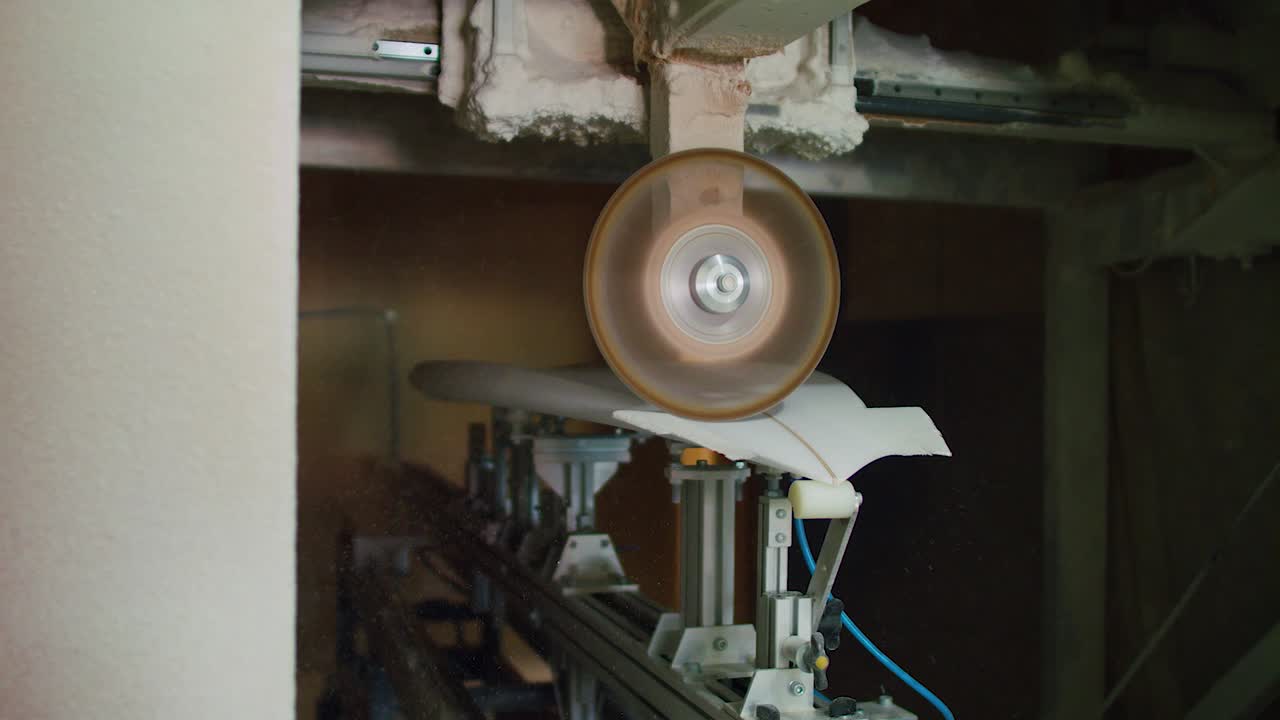 Surfboard is crafted by power planer in slow motion while dust moves around