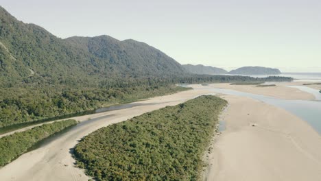 Aerial-orbiting-left-to-right-shot-of-a-sandy-beach-by-a-cliff-along-the-coastline-in-west-coast-New-Zealand