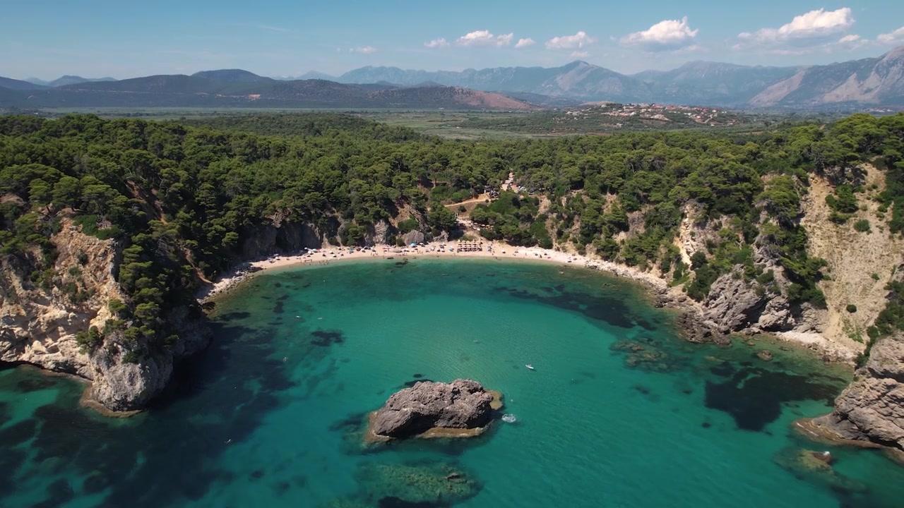 Ampia inquadratura paesaggistica della spiaggia di Alonaki Fanariou a Preveza, Grecia. Ripresa aerea che rivela acque limpide e un'isola rocciosa.