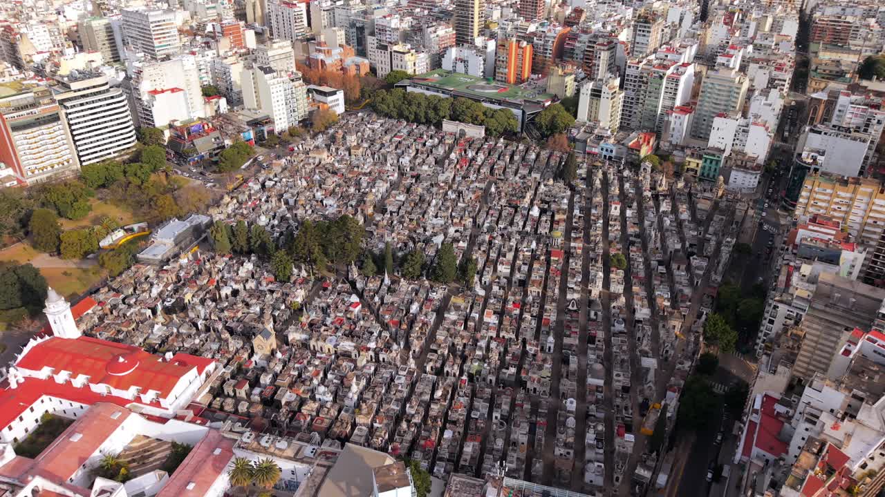 Il campo lungo mette in contrasto l'architettura compatta del cimitero con le strade circostanti e gli edifici di media altezza, sottolineando il Cimitero della Recoleta come un monumentale isolato urbano a Buenos Aires, in Argentina