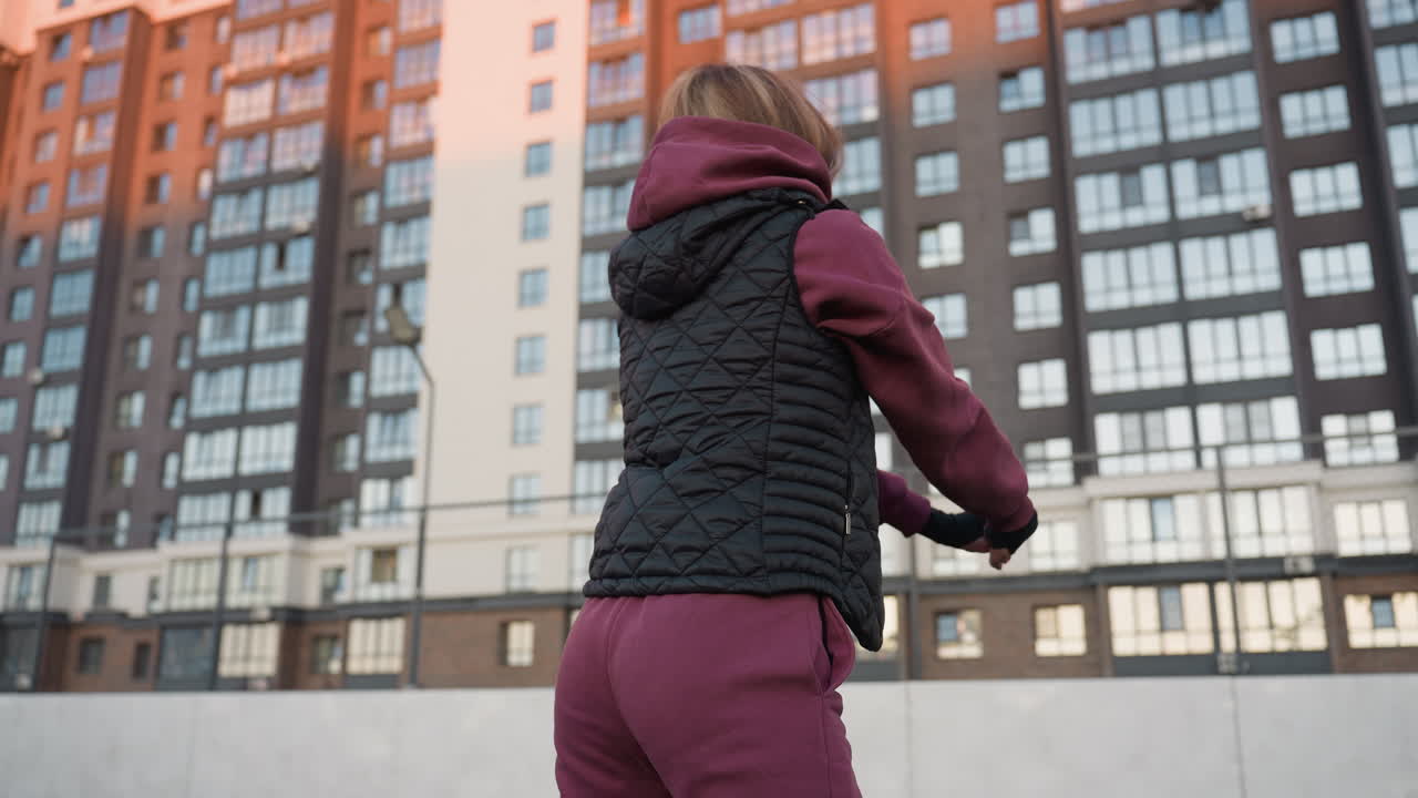 Back view female figure squatting on round sport court at sunset with warm glow on city high rise buildings showcasing strength stability balance in dusk light while city skyline looms behind
