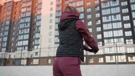 back view female figure squatting on round sport court at sunset with warm glow on city high rise buildings showcasing strength stability balance in dusk light while city skyline looms behind