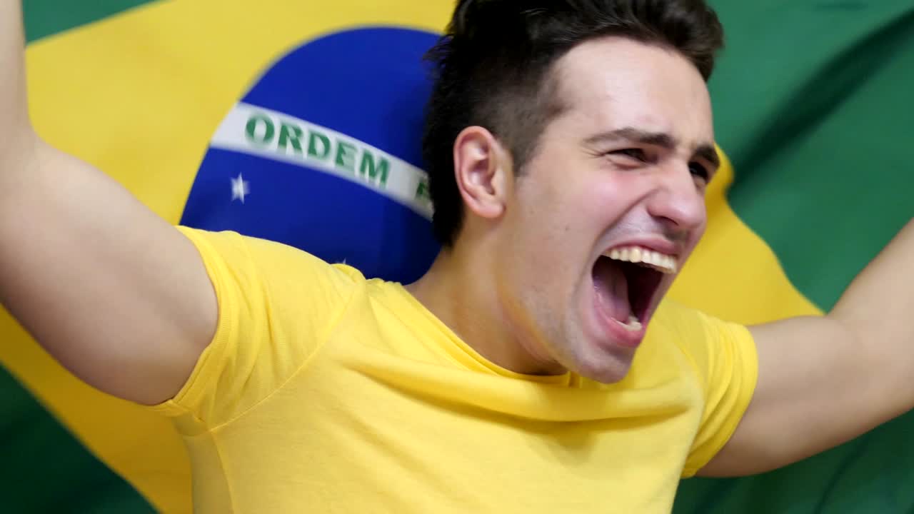 joven brasileño celebrando mientras sostiene la bandera de brasil en cámara lenta