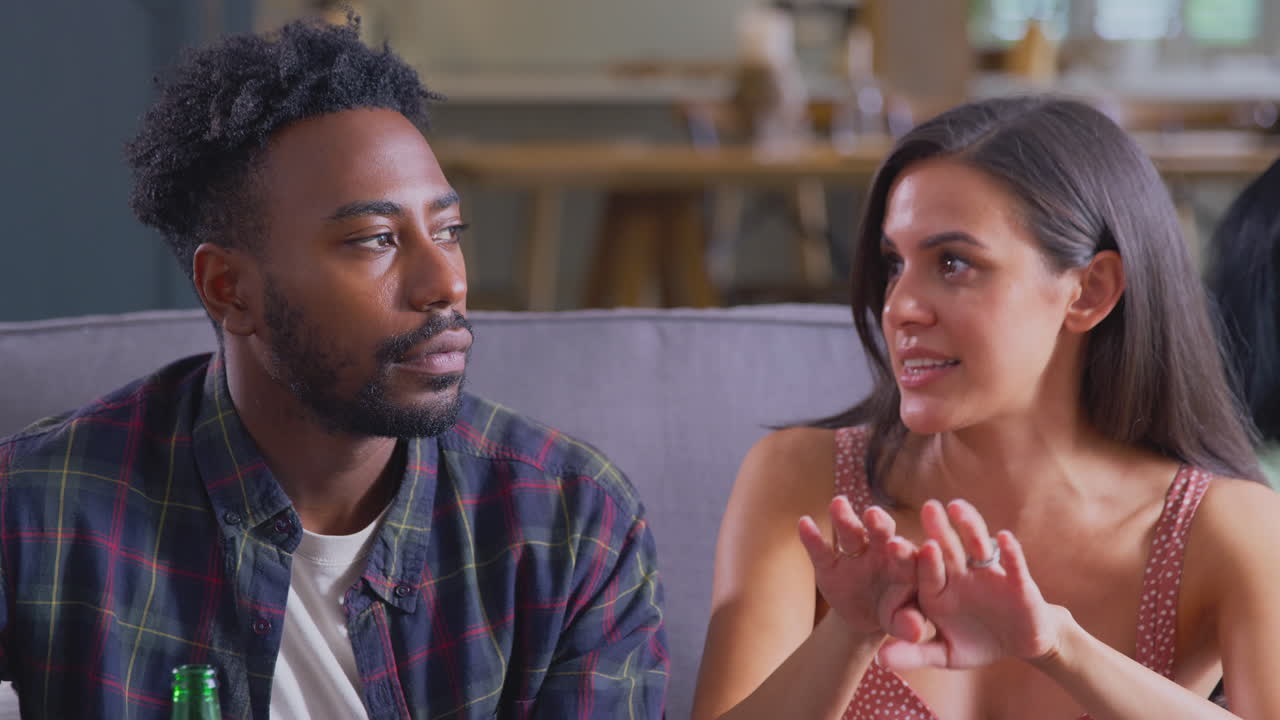 pareja joven sentada en el sofá en casa hablando y disfrutando de bebidas juntos