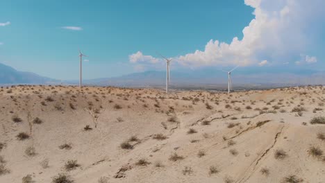 slow fly up and over of sand covered hills and windmills near small desert town