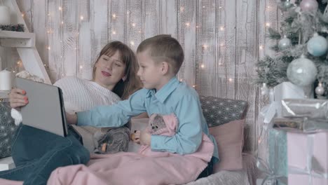 blond woman looks at little girl and boy switches on tablet