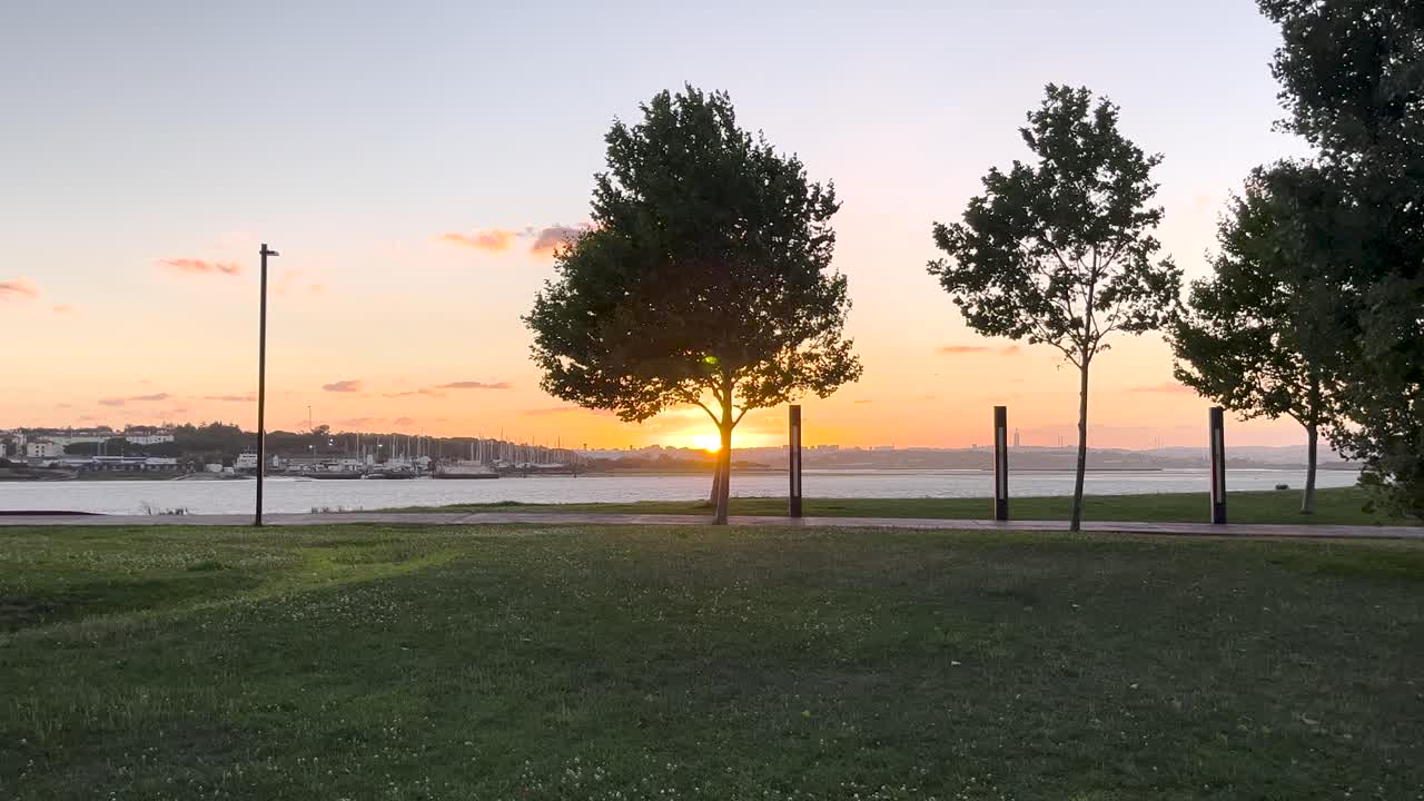 Sunset at park with silhouettes of trees and people walking, peaceful golden hour moment, slow zoom in