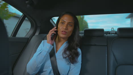 Mature-Businesswoman-Sitting-In-Back-Seat-Of-Taxi-Or-Car-Talking-On-Mobile-Phone