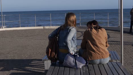 rear view of a caucasian and a mixed race girl talking sitting on a table