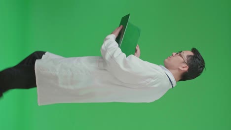 la vista lateral de un médico asiático con estetoscopio con gafas y abrigo blanco leyendo un documento mientras camina en pantalla verde con tecla de croma.