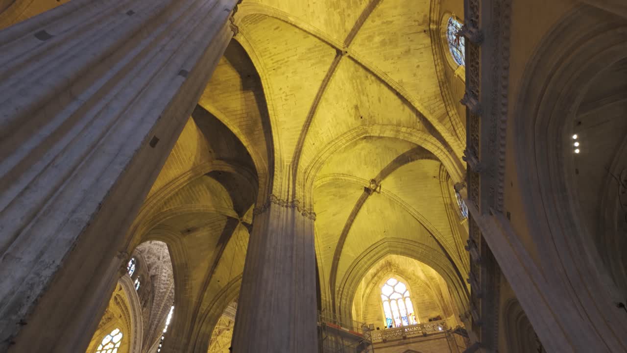 Interior view of Seville Cathedral, golden vaulted ceilings and detailed Gothic arches, tilt down