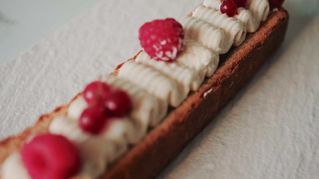 Close up of a gourmet pastry topped with cream, raspberries, and red currants