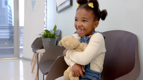 happy african american girl sitting in hospital waiting room and hugging mascot, slow motion