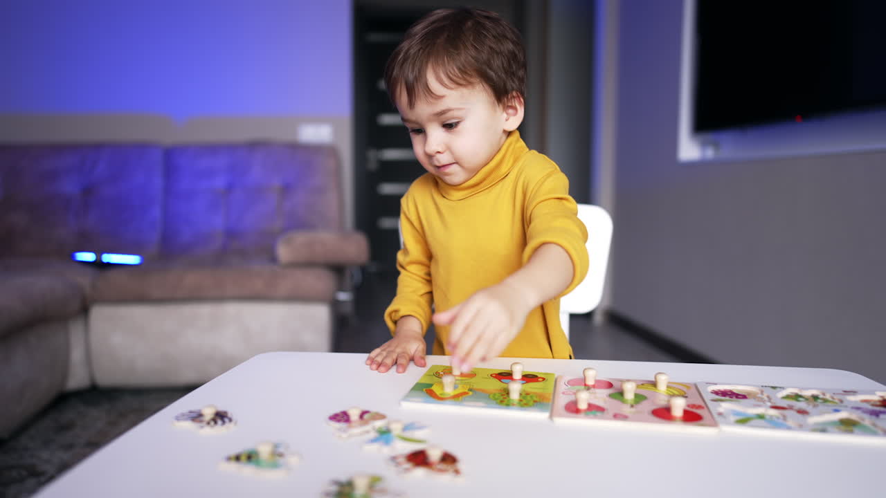 Cute little kid sits at desk tapping with his hands. Lovely toddler boy playing with puzzles and looking for necessary piece.