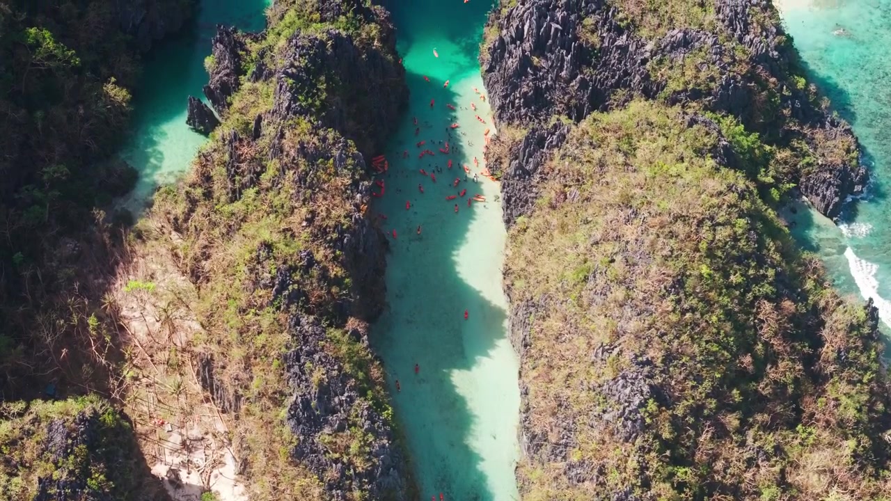 Turisti pagaiando in kayak attraverso una stretta laguna tropicale sotto scure scogliere carsiche.