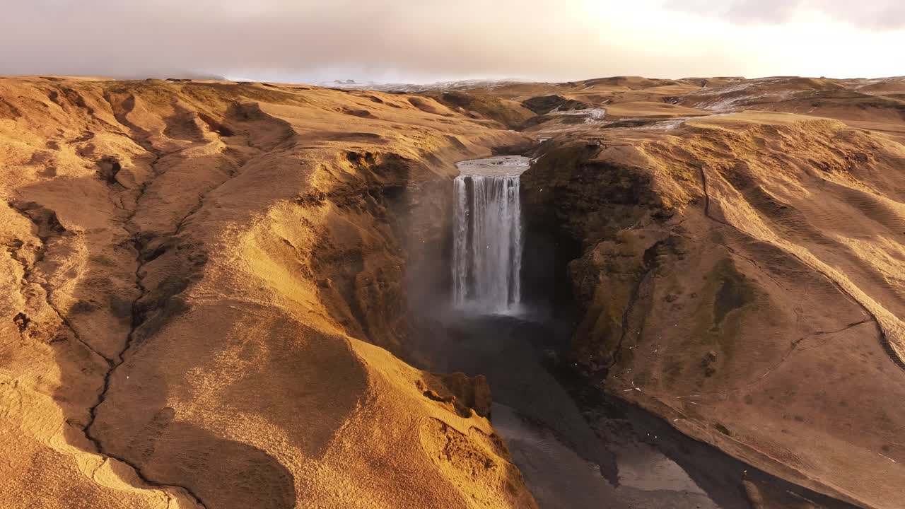 Majestic Skógafoss waterfall plunges through rugged Icelandic landscape. Moody, dramatic scene. Ideal for nature documentaries, travel vlogs, and scenic visuals.