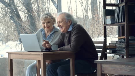 An-Older-Couple-Laughing-While-Looking-At-The-Laptop-Sitting-At-The-Table