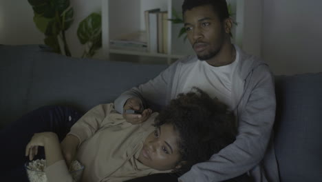 Young-Couple-Picking-A-Movie-With-The-Remote-Control-And-Eating-Popcorn-In-The-Dark