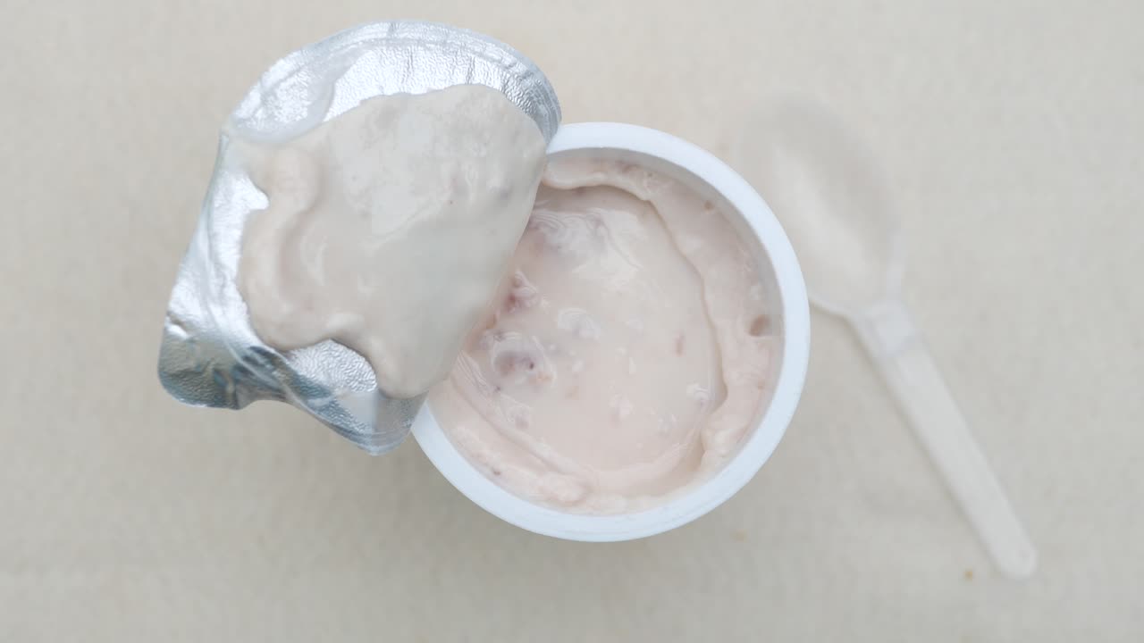 yogur fresco en un recipiente de plástico y una cuchara en la mesa