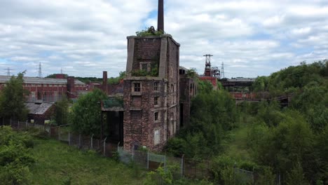 abandoned old overgrown coal mine rusting wheel derelict building aerial view low left orbit