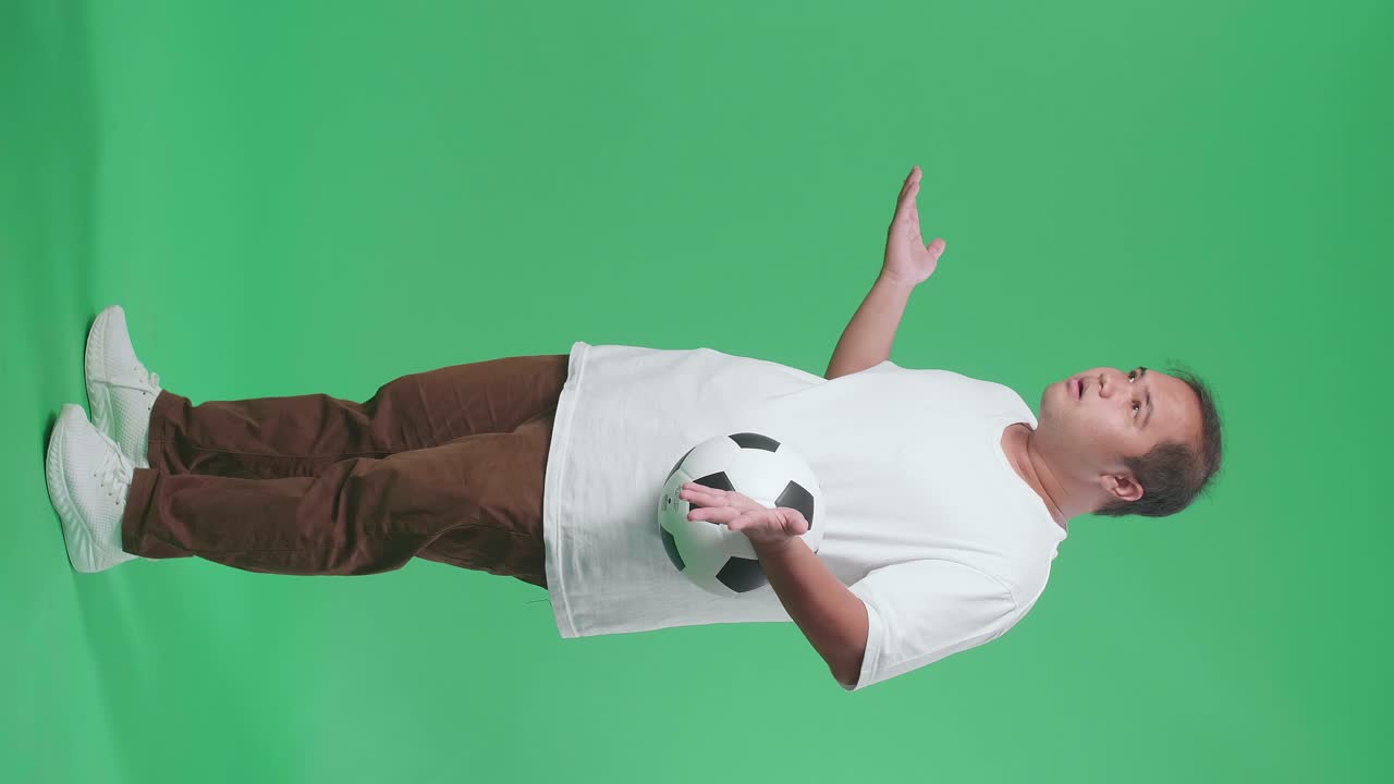 녹색 화면 배경에서 축구를 응원하는 동안 패자를 조롱하는 공을 가진 아시아 남자의 몸이 가득 차 있습니다.