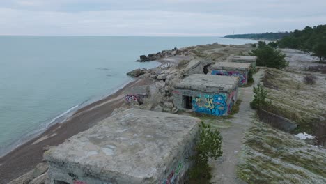 aerial view of abandoned seaside fortification buildings at karosta northern forts on the beach of baltic sea , waves splash, overcast day, wide ascending drone shot moving forward