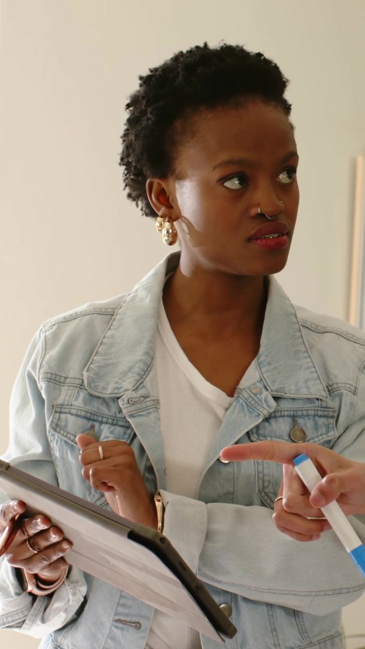 Video verticale: Donna che legge con giacca di jeans che tocca un tablet, seguendo un cursore a forma di mano blu in una stanza.
