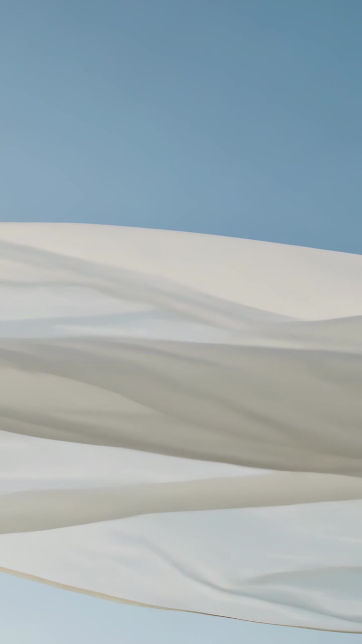 Video verticale: Tessuto bianco traslucido che si dispiega e fluttua nel cielo azzurro e limpido, spinto dal vento.