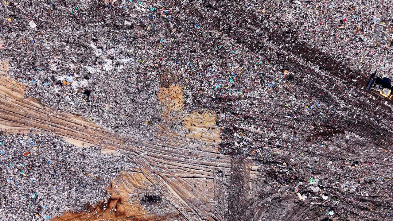 Vista aérea zenital de lixo e detritos compactados com trilhas de trator de esteira na superfície de um aterro sanitário. Textura aérea em detalhe de resíduos municipais não triados.