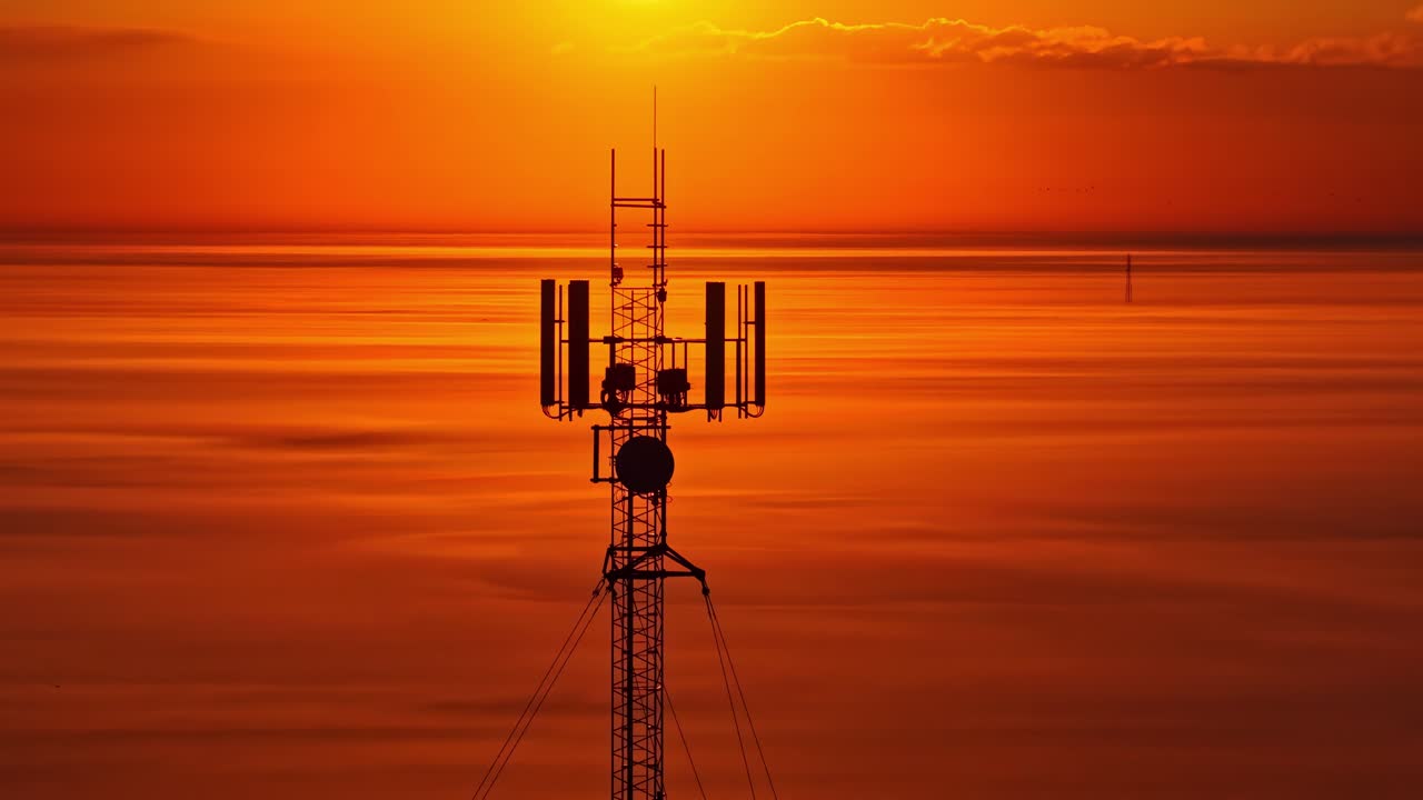 Cell tower with bright sunlight glowing behind it, filmed by drone
