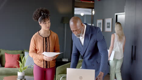 Diverse-business-people-discussing-using-laptop-in-office-with-copy-space