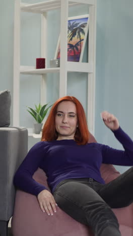 red-haired housewife comes to sit on bean bag chair to rest after domestic chores. happy woman enjoys relaxing in living room at home slow motion