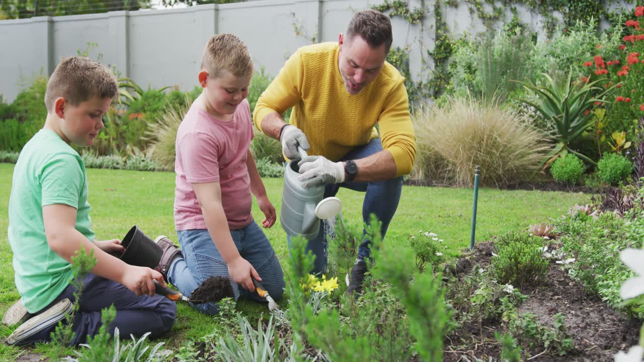 padre caucásico feliz con dos hijos haciendo jardinería juntos y regando plantas en el jardín