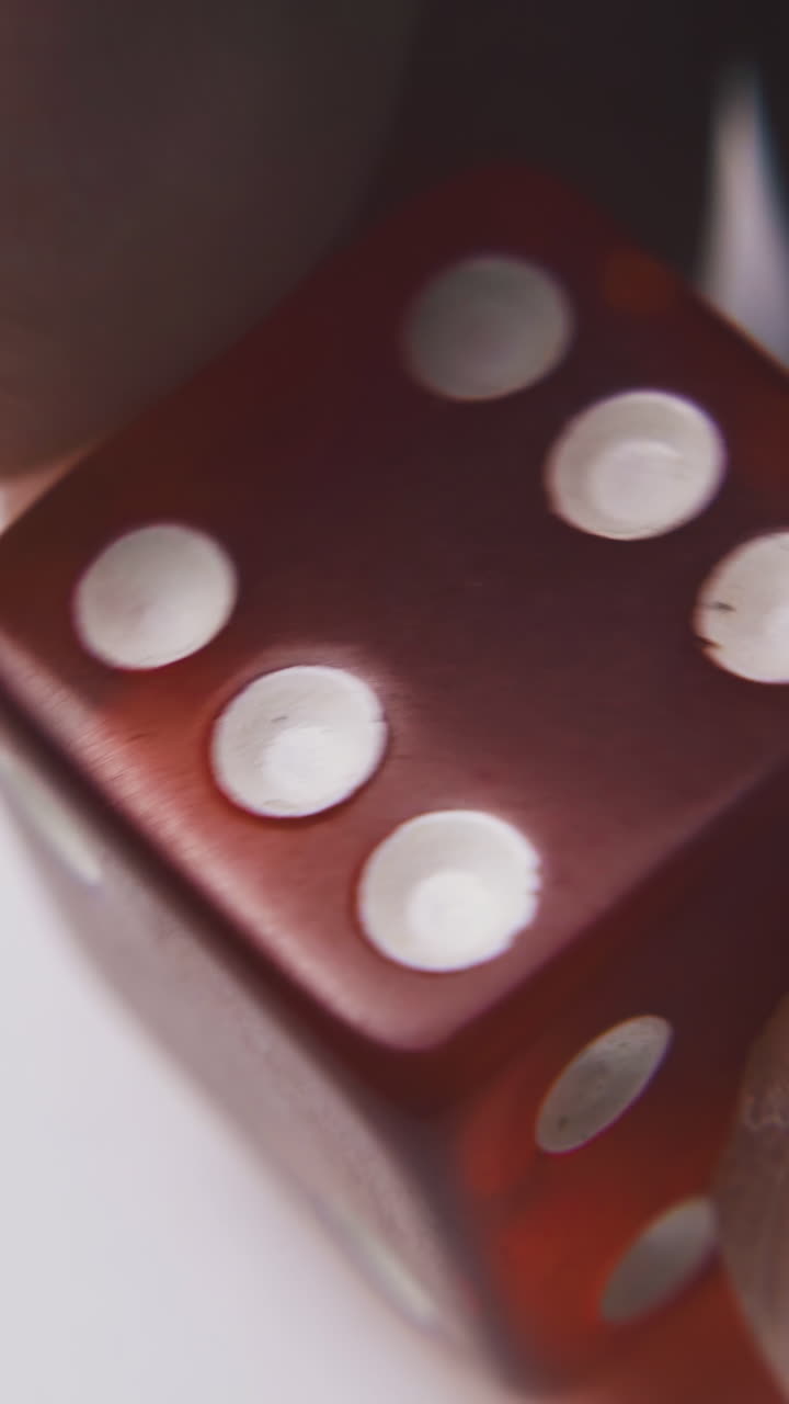 person turns bright red plastic dice with white spots on sides against light background macro