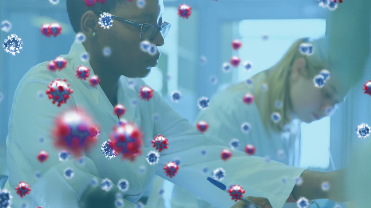 Sich bewegende Covid-19-Zellen vor zwei Wissenschaftlerinnen, die im Labor arbeiten.