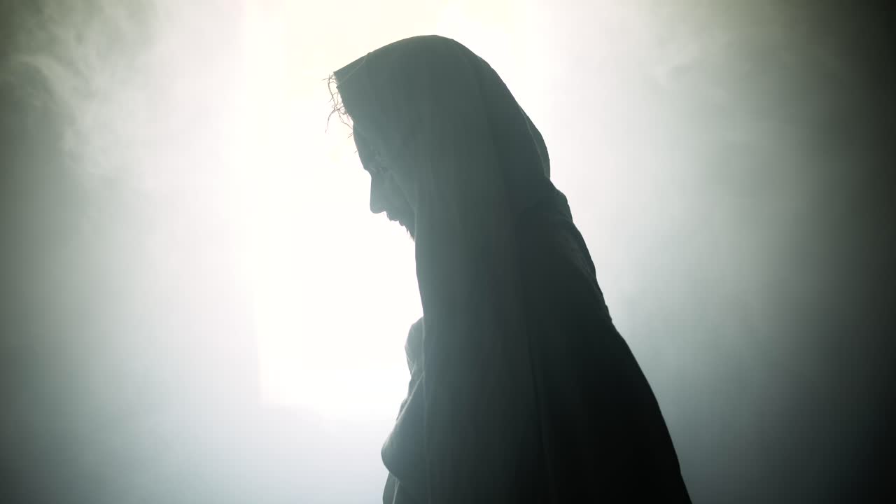 Silhouette of the resurrected Jesus Christ standing inside the tomb in bright, dramatic, holy light as representation of the Easter Sunday resurrection in cinematic slow motion.