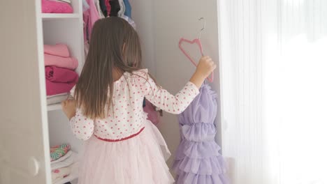 a little girl is choosing a dress in the wardrobe.