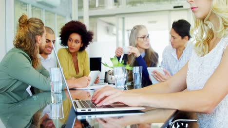 Woman-using-laptop-while-colleagues-interacting-in-background-4k