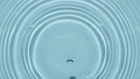 top view slow motion of drop falls into water and diverging circles of water on blue background. water drop splash blue colored. 4k