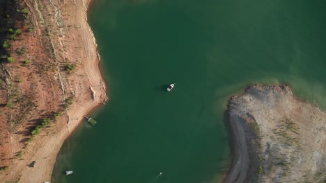 drone descending towards isolated little boat in water reservoir at sunset