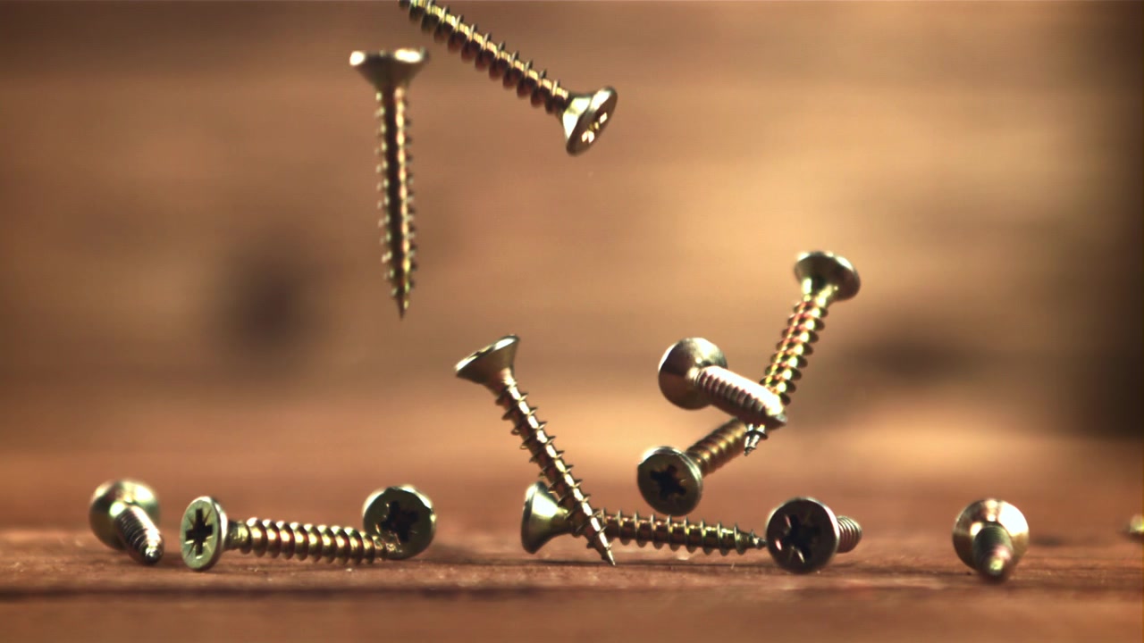 Golden Metal Screws Falling onto a Wooden Surface in Slow Motion