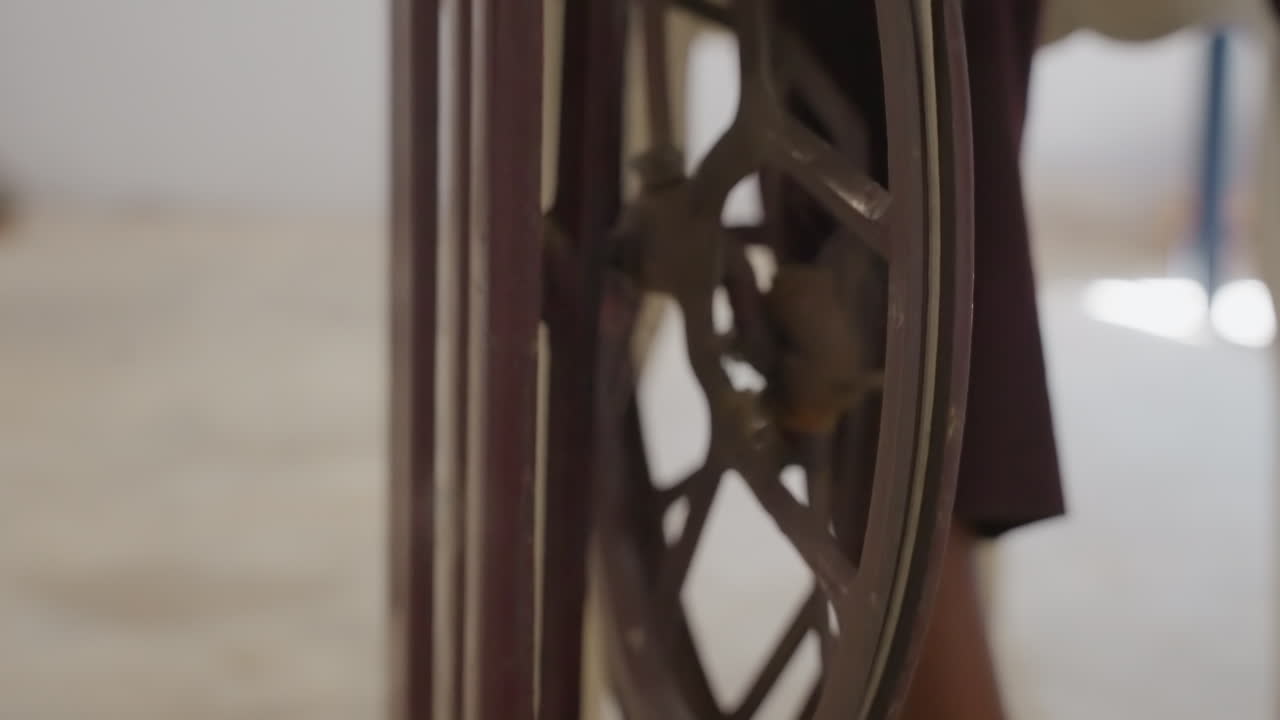 Primo piano di ruota da cucire con tessuto nero, interni luminosi che incorniciano un volano antico e una cornice di legno, azione implicita di sarta che regola tessuto e modello, vivace scena di riparazione domestica con sguardo concentrato