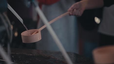 Chozuya---El-Devoto-Usa-Un-Cucharón-De-Madera,-Hishaku-Para-Verter-Agua-Sobre-Sus-Manos-Dentro-De-Un-Pabellón-En-Un-Santuario-Japonés