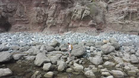 camión siguiendo la antena de un hombre con una mochila amarilla caminando a lo largo de la costa atravesando rocas y rocas oceánicas aventurándose con un espectacular acantilado en el fondo