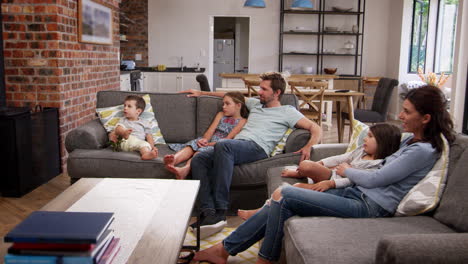 family sit on sofa in open plan lounge watching television