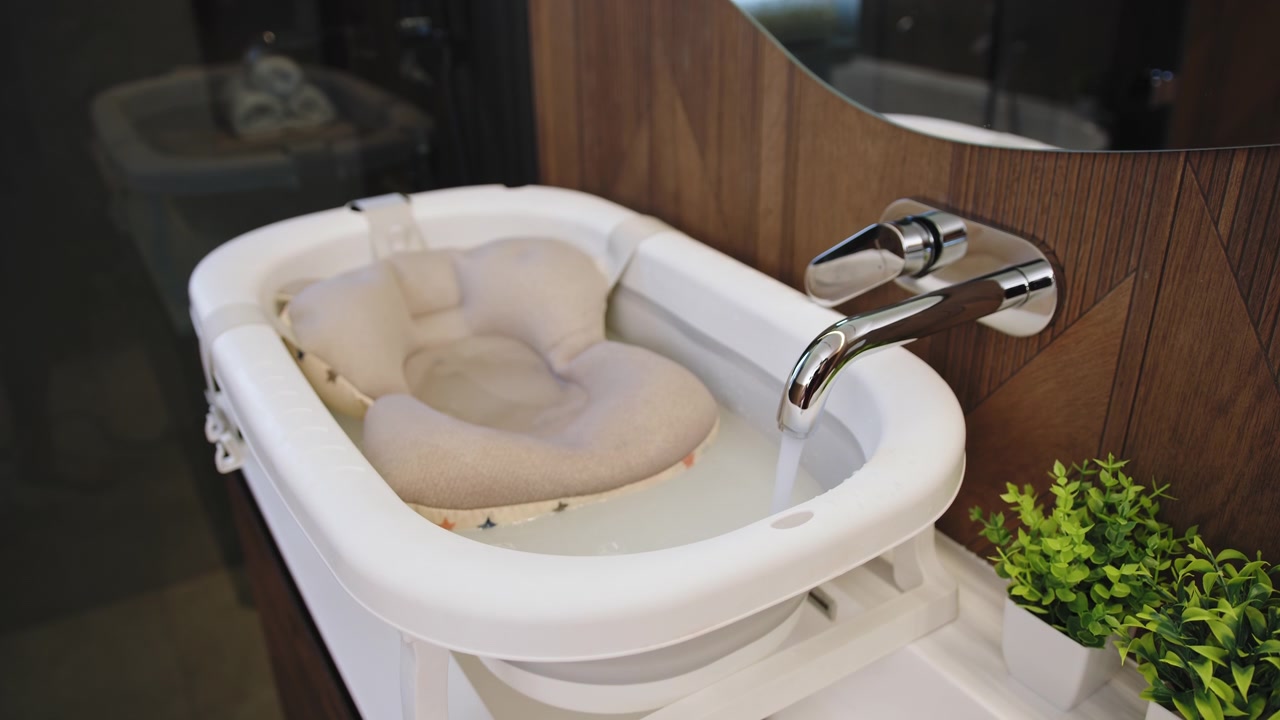 Closeup of a baby bathtub with water filling from a chrome faucet featuring a soft cushion and