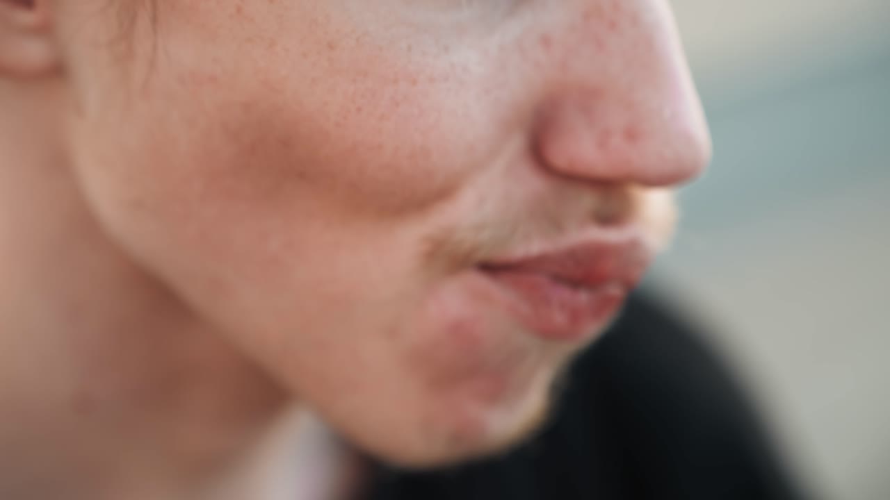 Primo piano di giovane skater che sorride maliziosamente durante l'allenamento in strada, sorriso sottile con baffi e barba incolta, sfondo bokeh morbido, atmosfera diurna che trasmette energia giovanile e giocosa e fascino spontaneo.