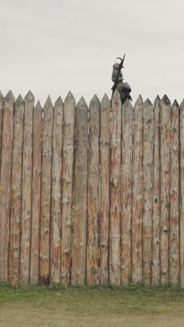 brave warrior patrols border of settlement walking along high wooden picket fence rain. medieval sentry in knightly armor inspects territory standing on rise