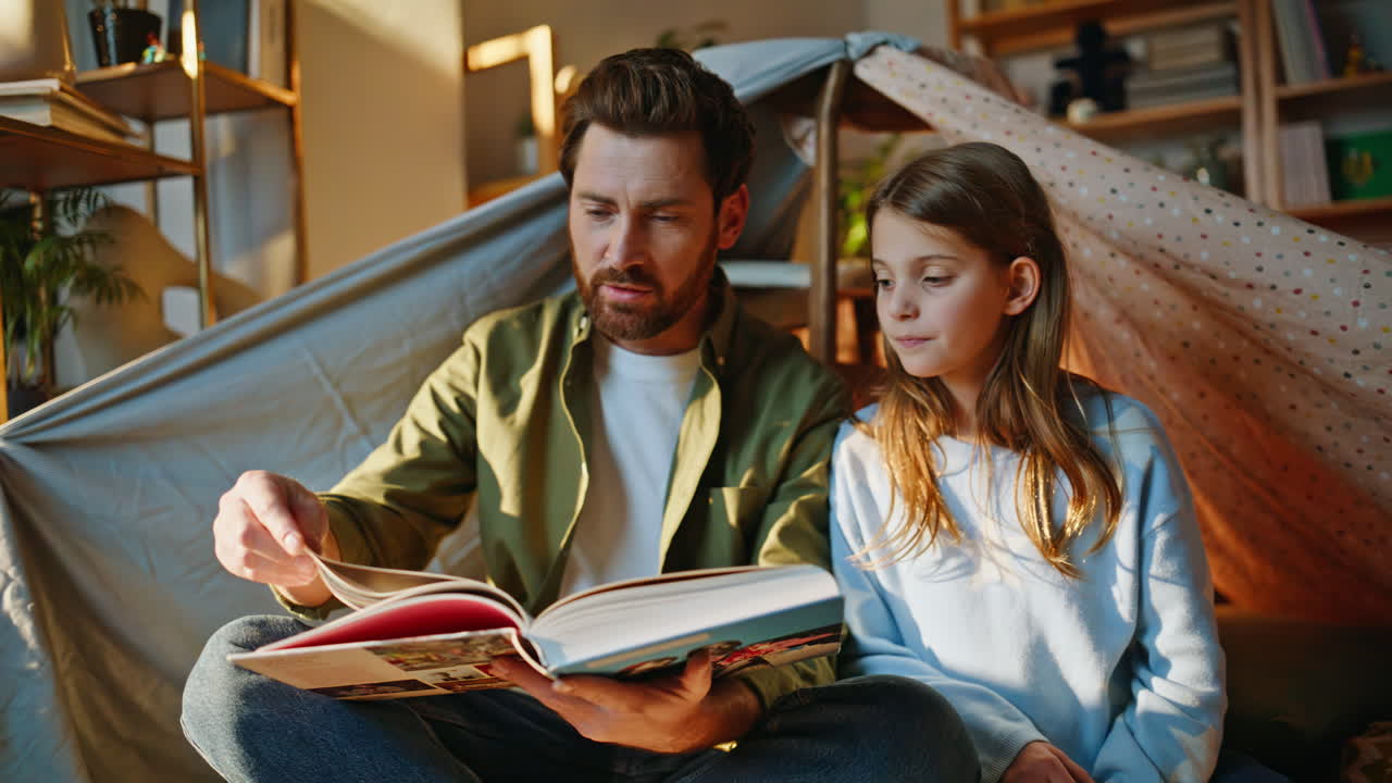 Padre single legge un libro a un bambino in una fortezza di coperte, primo piano. Genitore che racconta una storia